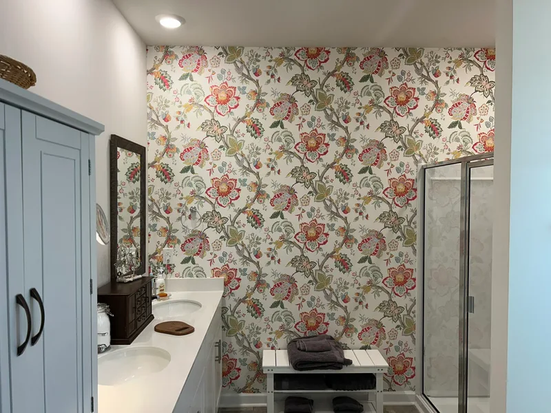 This charming bathroom features a vibrant chinoiserie-inspired floral wallpaper with twisting branches laden with oversized, multicolored blooms in rich reds, corals, pinks, and sunny yellows, accented by lush green leaves and subtle foliage details. Set against a soft cream or light neutral background, the intricate, repeating pattern evokes classic elegance with a fresh, lively twist—blending exotic botanical charm and timeless sophistication. Perfect as a bold accent wall, this design brings warmth, personality, and a touch of romantic flair to any space, making it an ideal choice for bathrooms, powder rooms, or cozy retreats seeking standout style. (Installed to stunning effect in a local Greer-area home!)