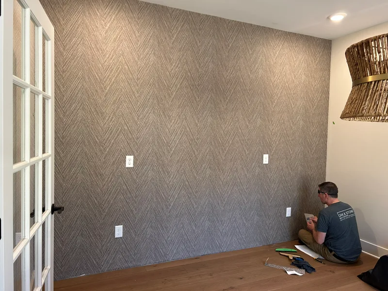This striking office accent wall showcases a modern faux grasscloth wallpaper in a sophisticated chevron pattern. The textured, linear design in neutral gray tones creates depth and visual interest, transforming the space into a refined and contemporary workspace